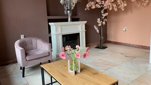 Un salon avec une cheminée blanche, un fauteuil rose, une table basse en bois et un vase rempli de fleurs roses.