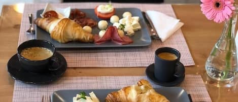 A breakfast setting with croissants, tomatoes, cheese, and a flower vase on a table.