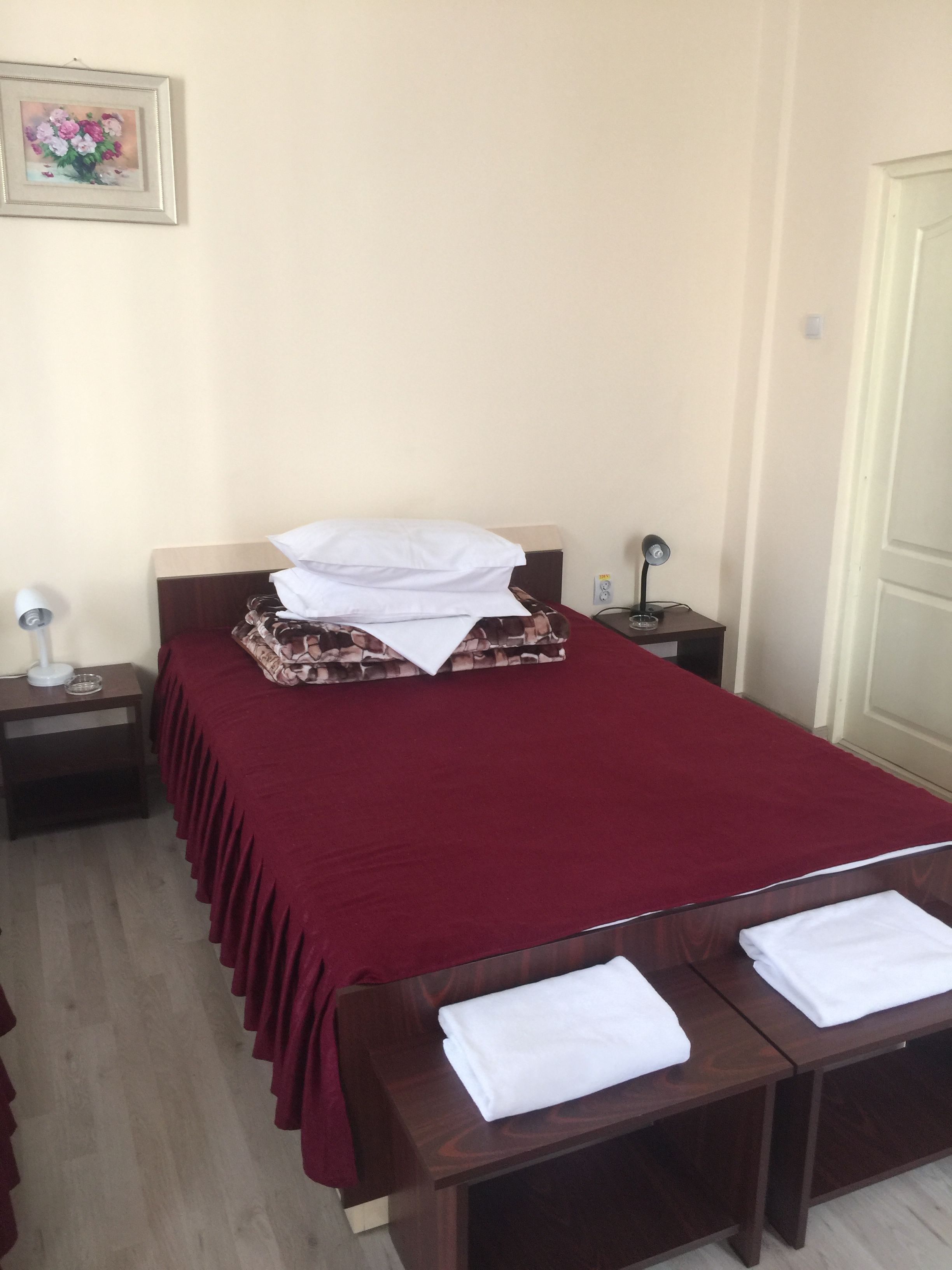 A neatly made bed with a red bedspread, two white pillows, and a folded blanket on a wooden nightstand.