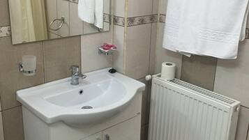 Un baño con un lavamanos blanco, un espejo, un perchero para toallas, un sujetapapeles y un radiador.