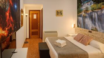 Una habitación de hotel con cama, escritorio, silla, puerta y un cuadro de una cascada.