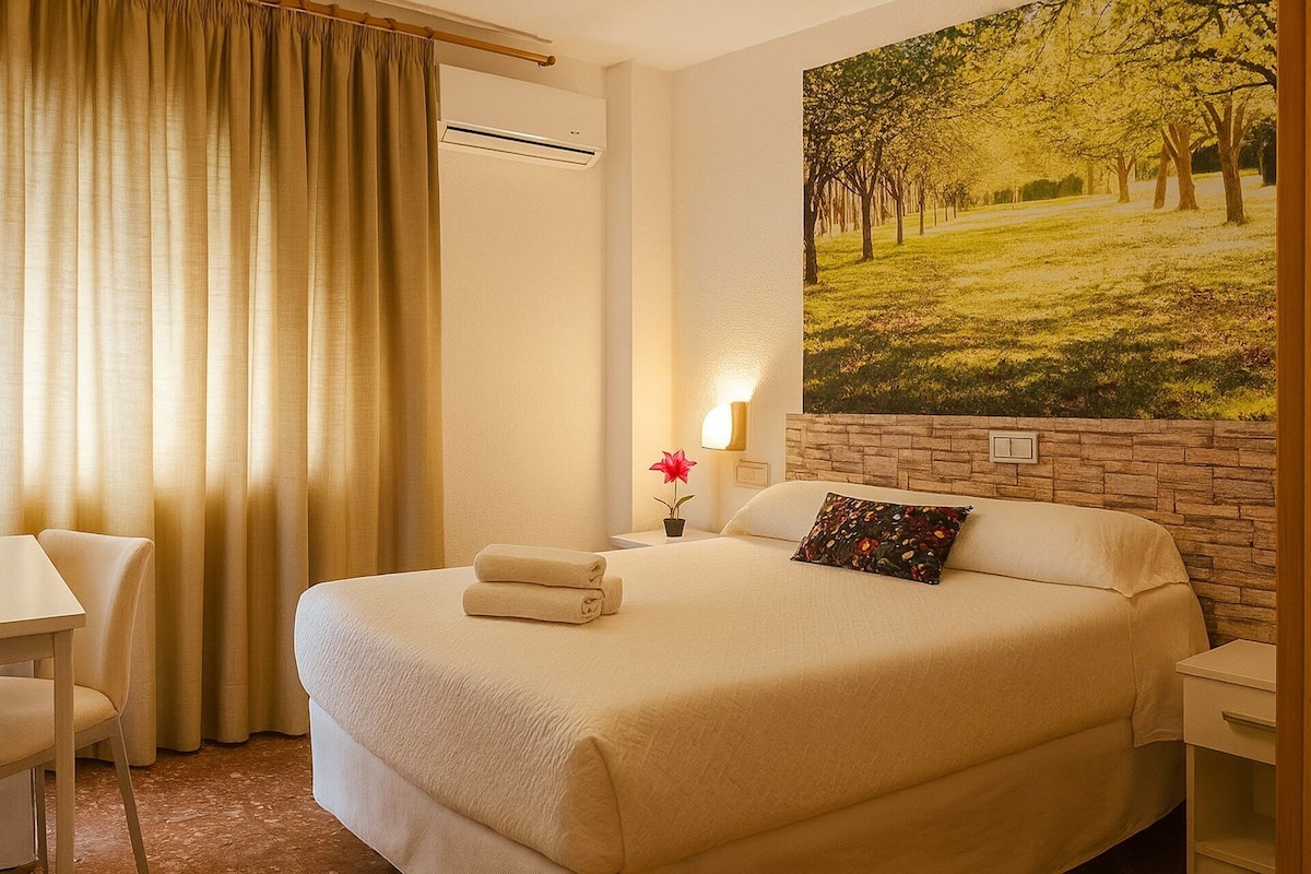 A hotel room with a large bed, a desk, and a painting of a park.