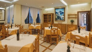Un comedor con varias mesas y sillas, un cuadro grande en la pared y vistas al exterior a través de las ventanas.
