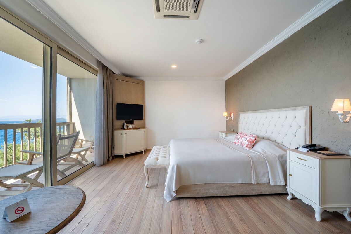A bedroom with a large bed, a bedside table, a TV, a nightstand, and a balcony with a view.