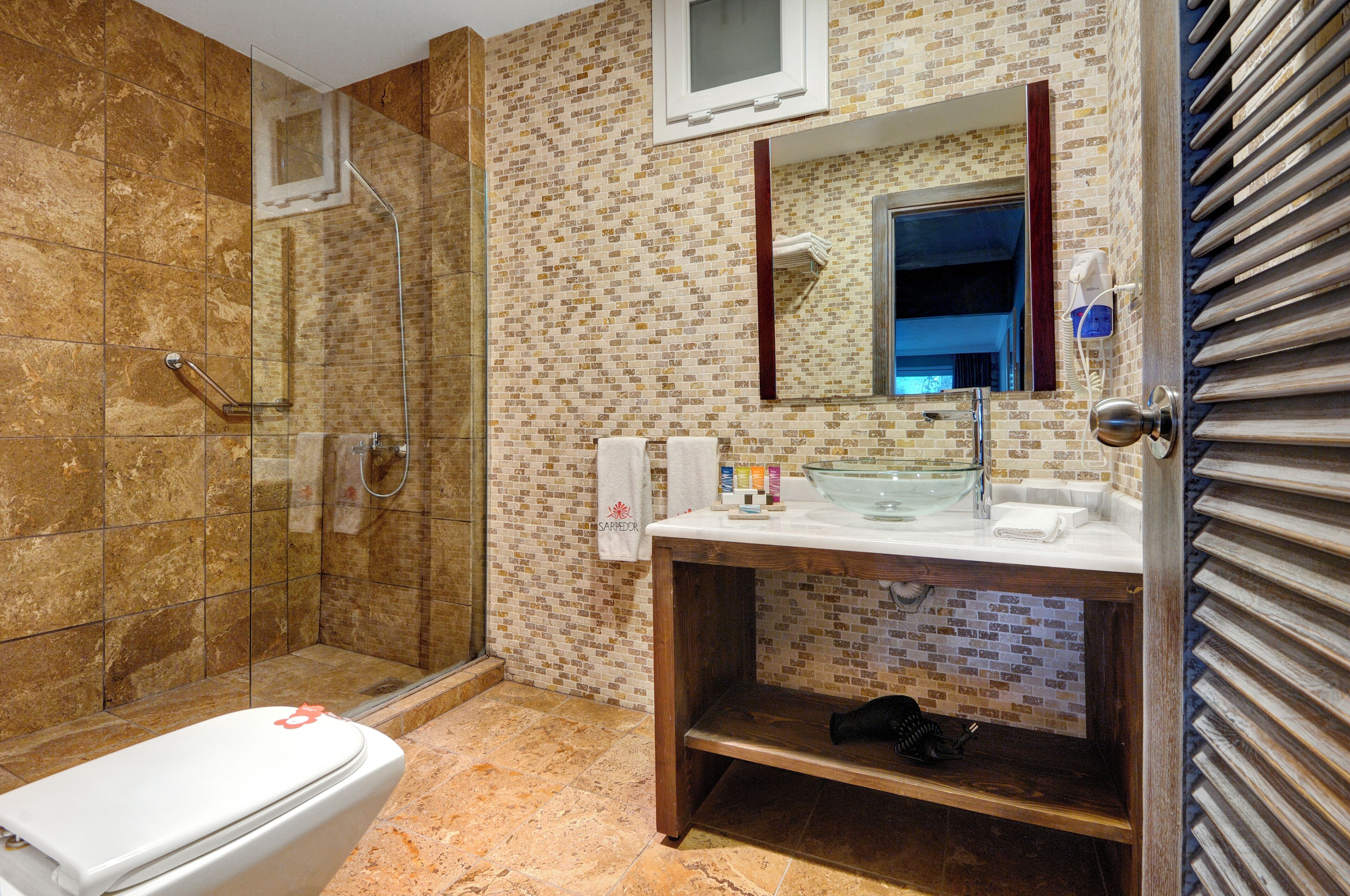 A bathroom with a glass shower enclosure, a white toilet, a sink with a mirror, and a towel rack.