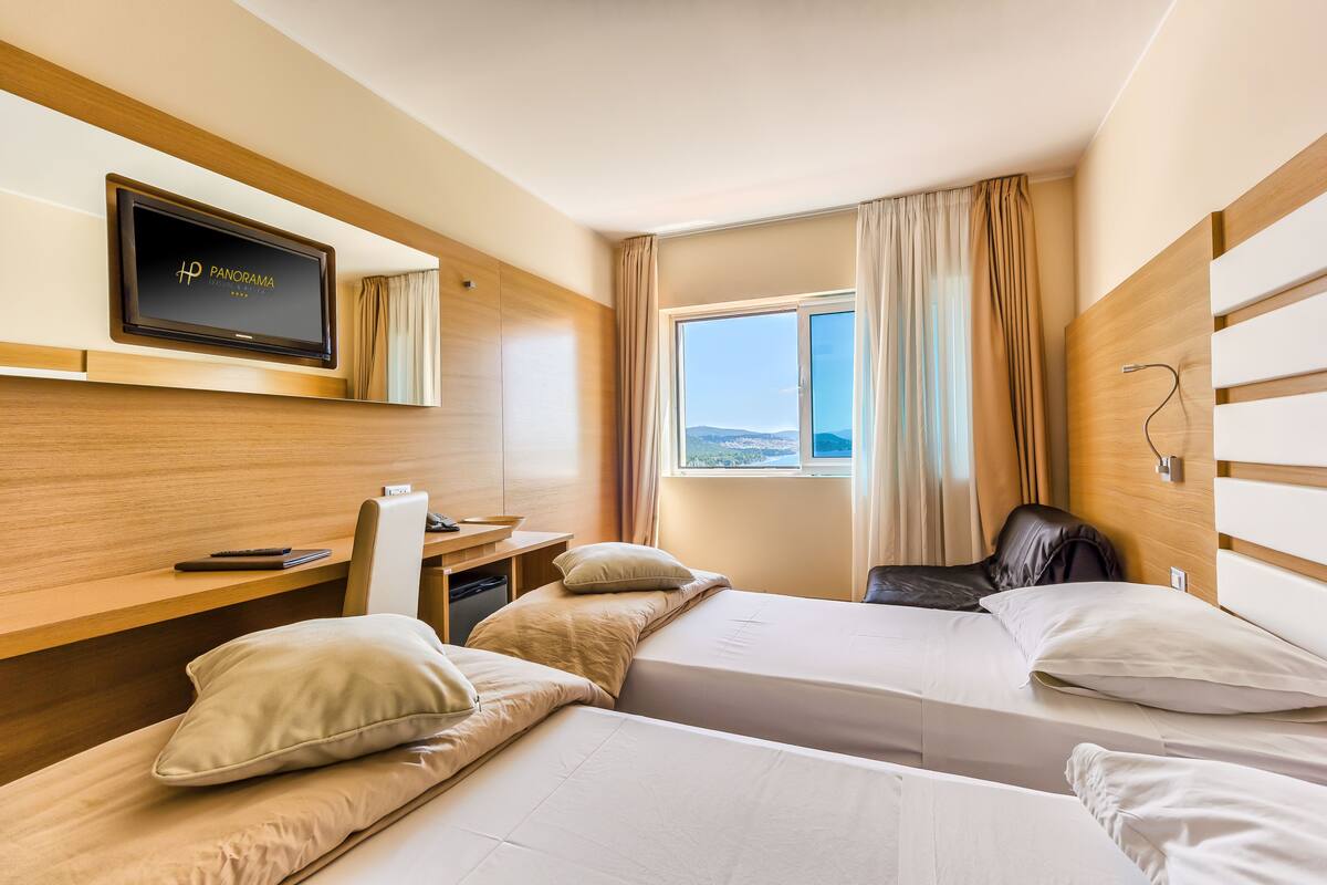 A hotel room with two beds, a desk, a television, and a window with a view.