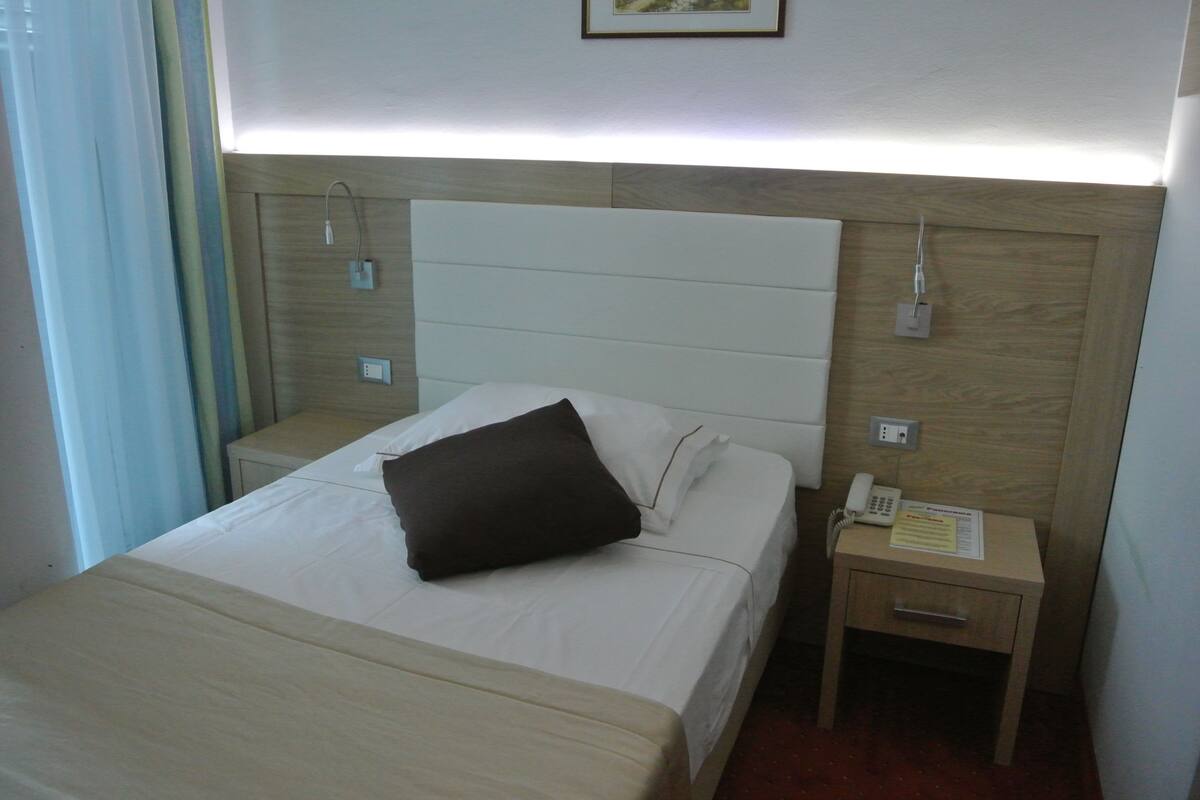 A hotel room with a bed, a bedside table with a phone, and a wall socket.
