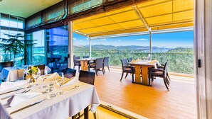 A restaurant with outdoor seating, a view of the mountains, and a large window. - Hotel Panorama (Sibenik)