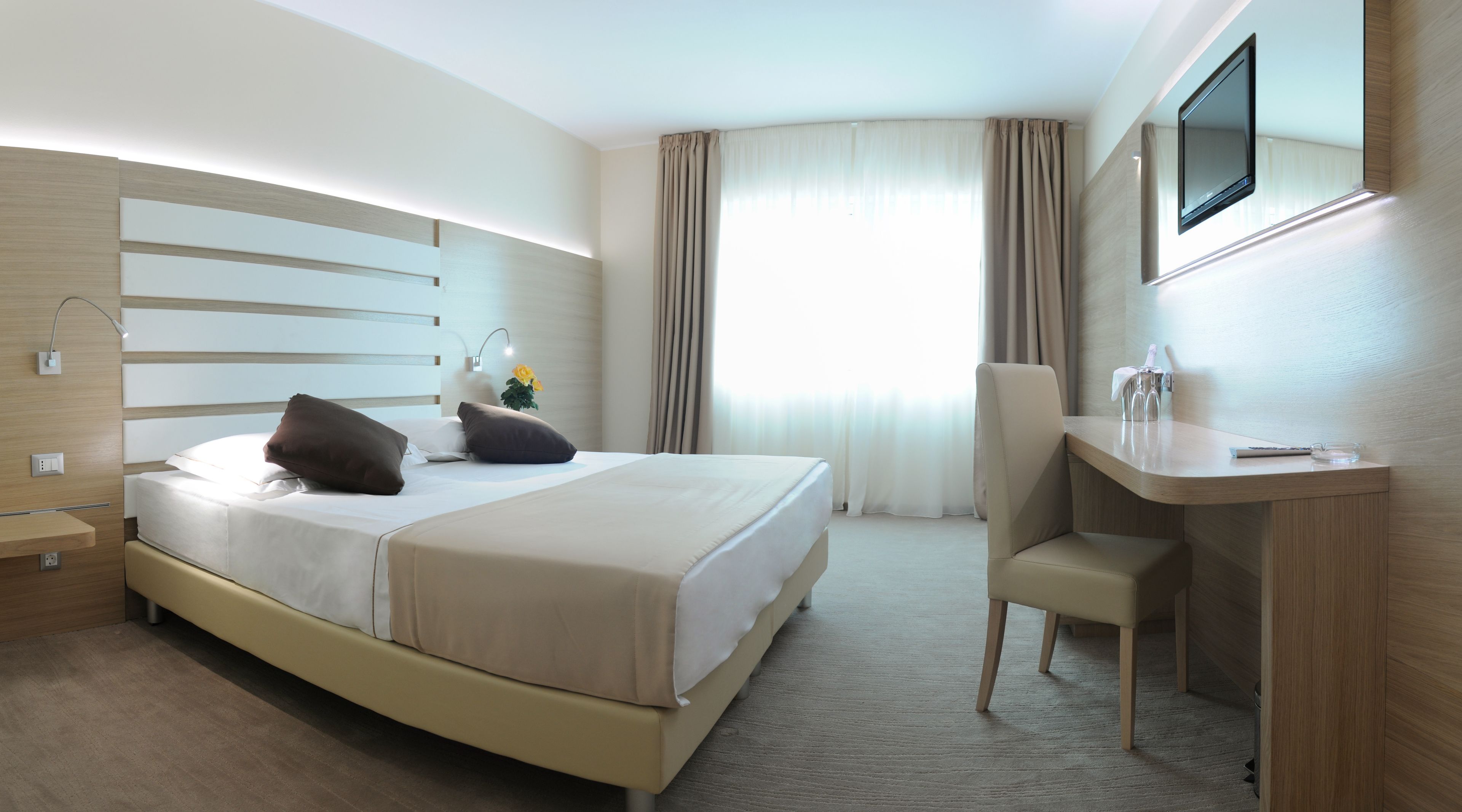 Ein Hotelzimmer mit Bett, Nachttisch, Sessel und einem an der Wand befestigten Fernseher.