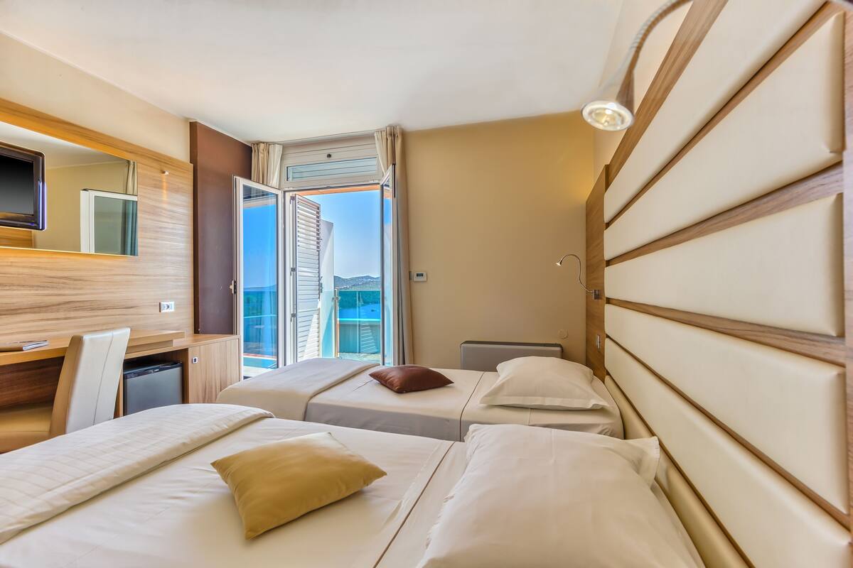 A hotel room with two beds, a desk, a TV, and a window with an open door.