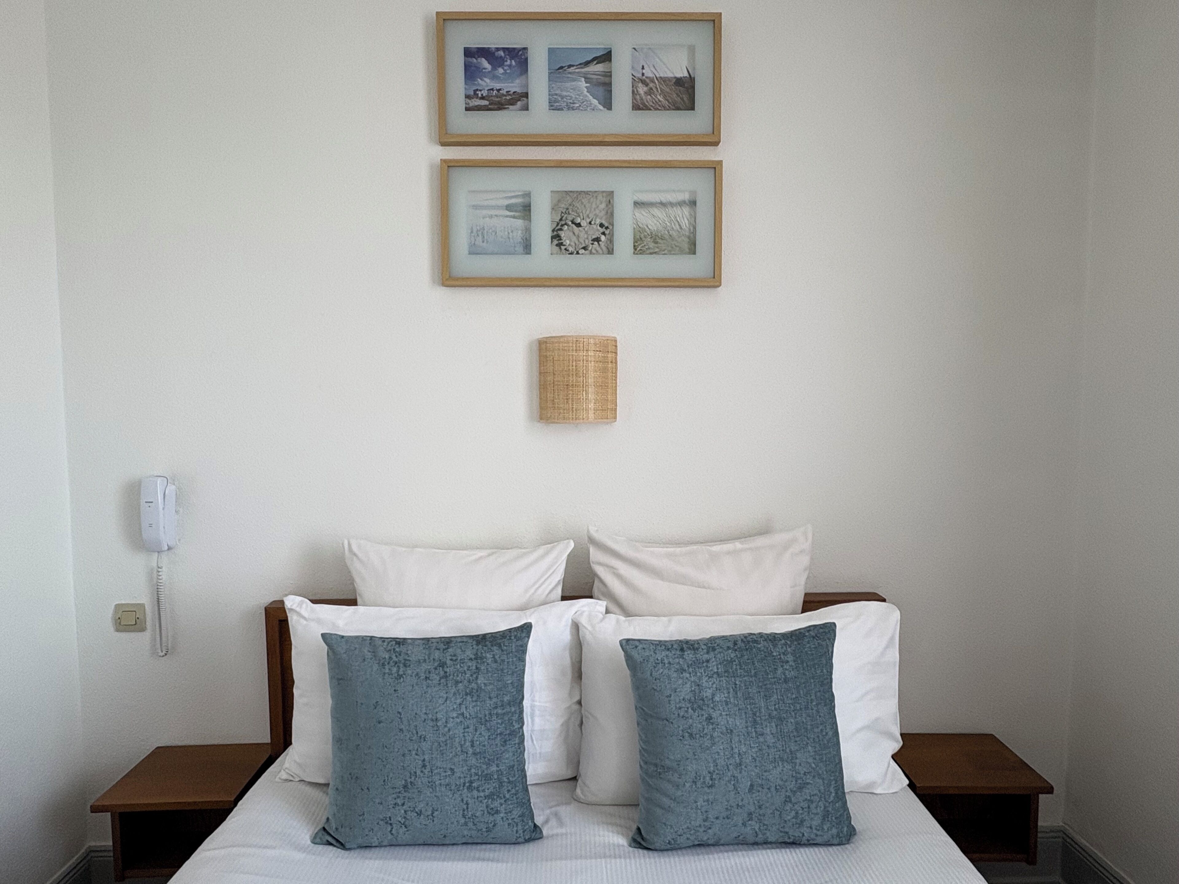 Une chambre à coucher avec un lit, deux oreillers, une table de chevet, une lampe et deux tableaux encadrés accrochés au mur.