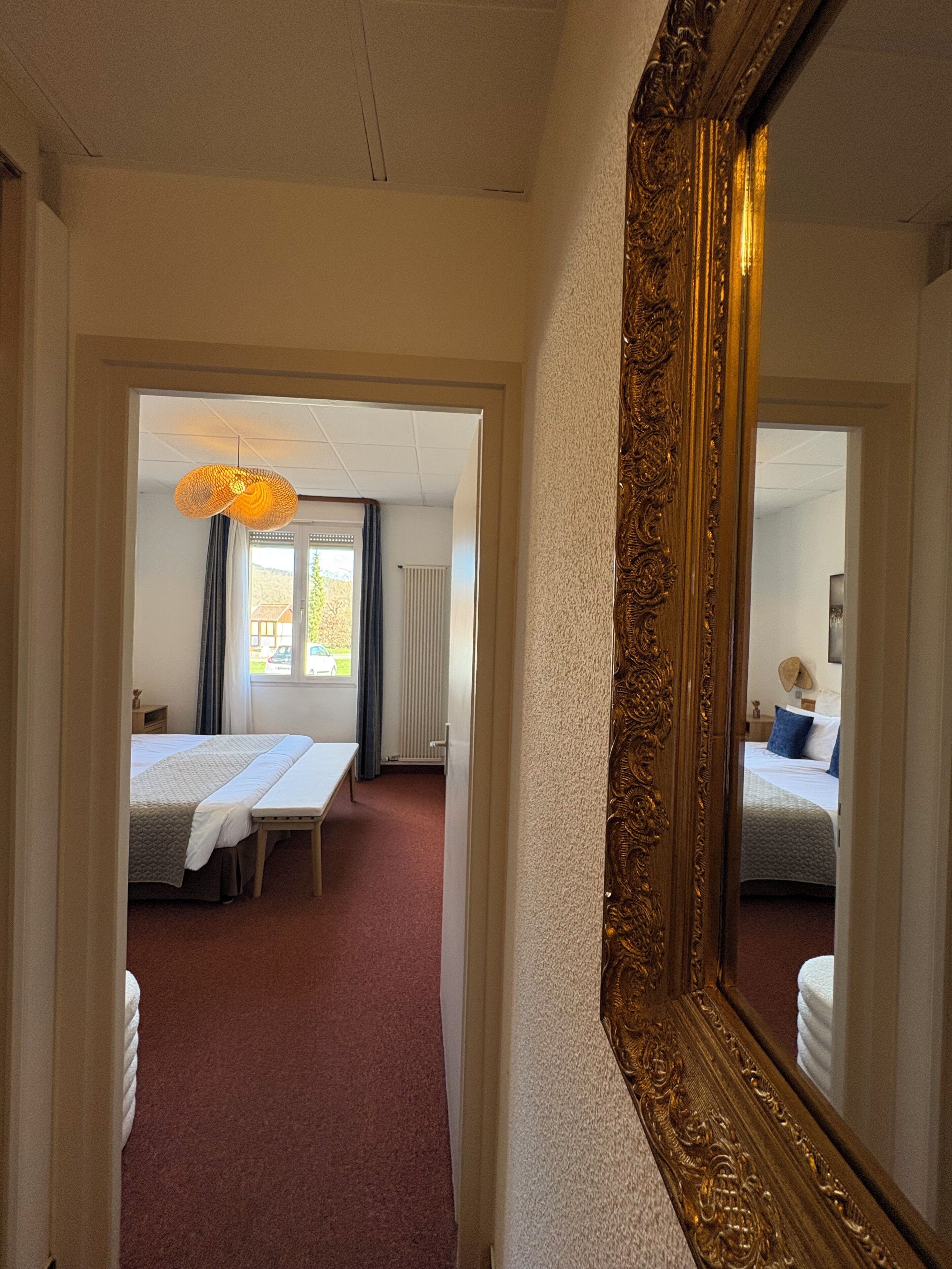 A hotel room with a large mirror, a bed, a desk, and a window with curtains.