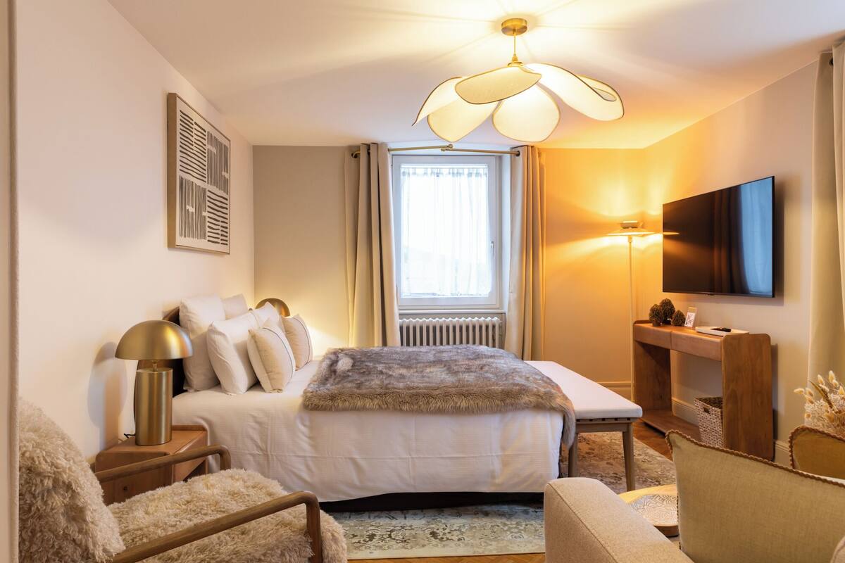 A hotel room with a bed, a desk, a television, and a window with curtains.