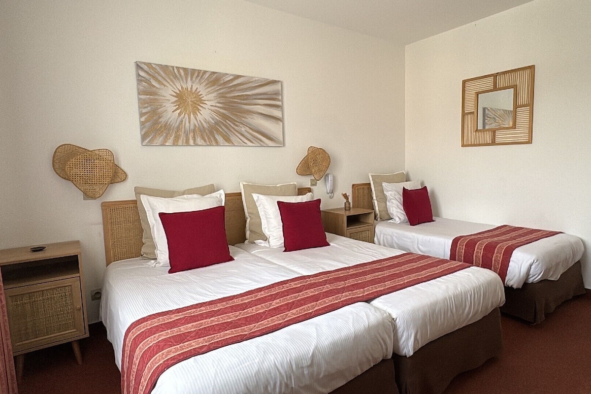A double room with two beds, a bedside table, a nightstand, a wall-mounted mirror, and a decorative wall piece.