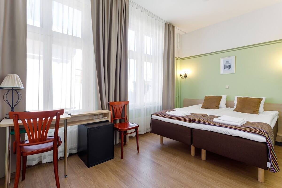 A hotel room with a bed, two chairs, a desk, and a lamp.