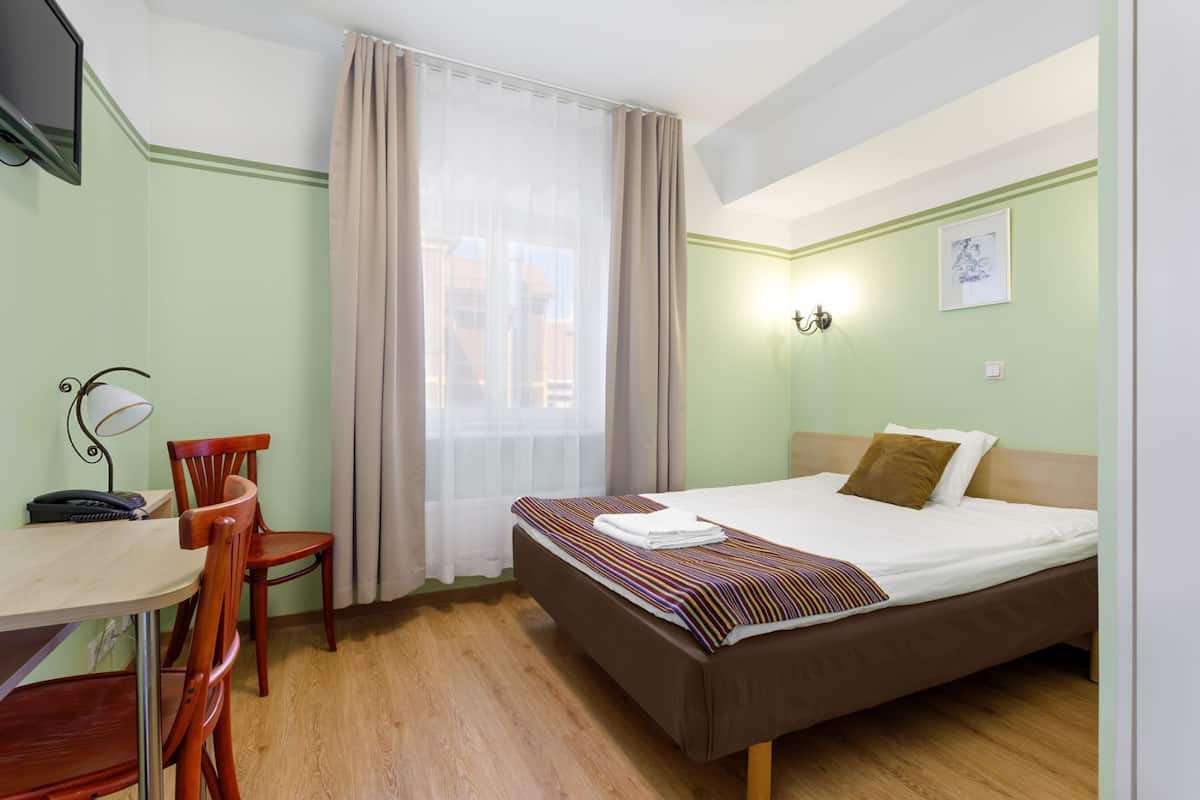A hotel room with a bed, a desk with a chair, a telephone, and a window with curtains.
