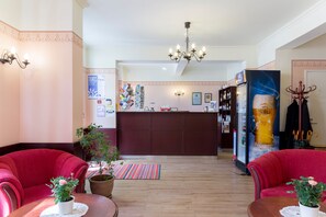 A hotel lobby with a reception desk, red chairs, a chandelier, and potted plants. - Koidulapark Hotell (Parnu)