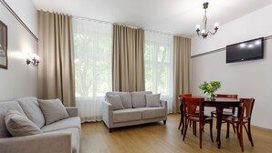 A modern living room with a sofa, a dining table with chairs, and a TV mounted on the wall. - Koidulapark Hotell (Parnu)