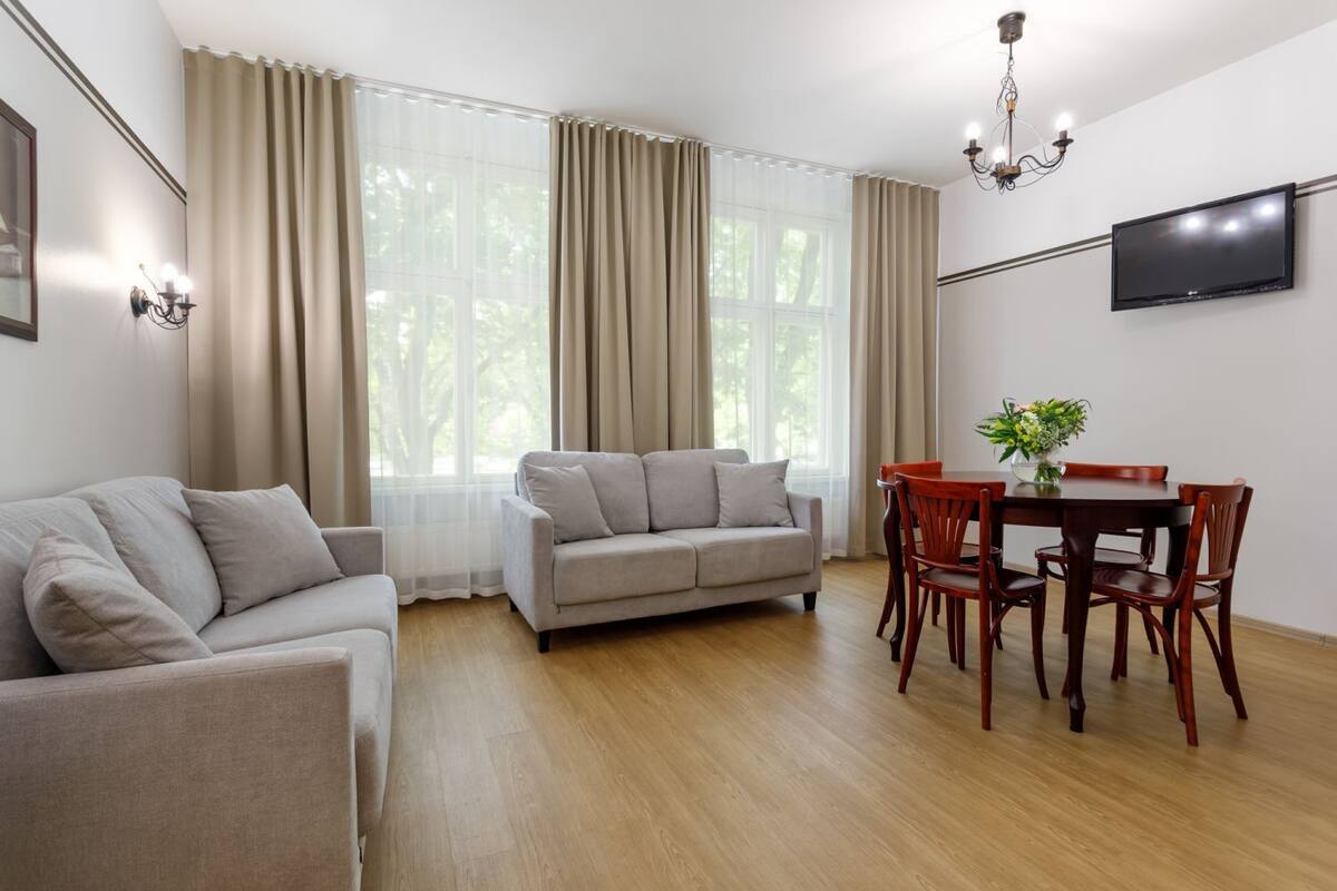A modern living room with a sofa, a dining table with chairs, and a TV mounted on the wall.