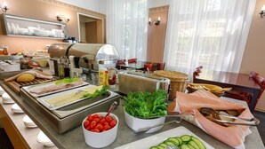 A buffet setup with various food items, including sliced cucumbers, cherry tomatoes, and leafy greens. - Koidulapark Hotell (Parnu)