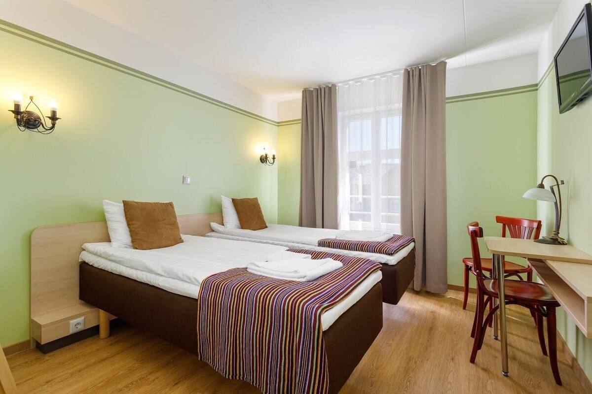 A hotel room with two beds, a desk, a chair, and a TV.