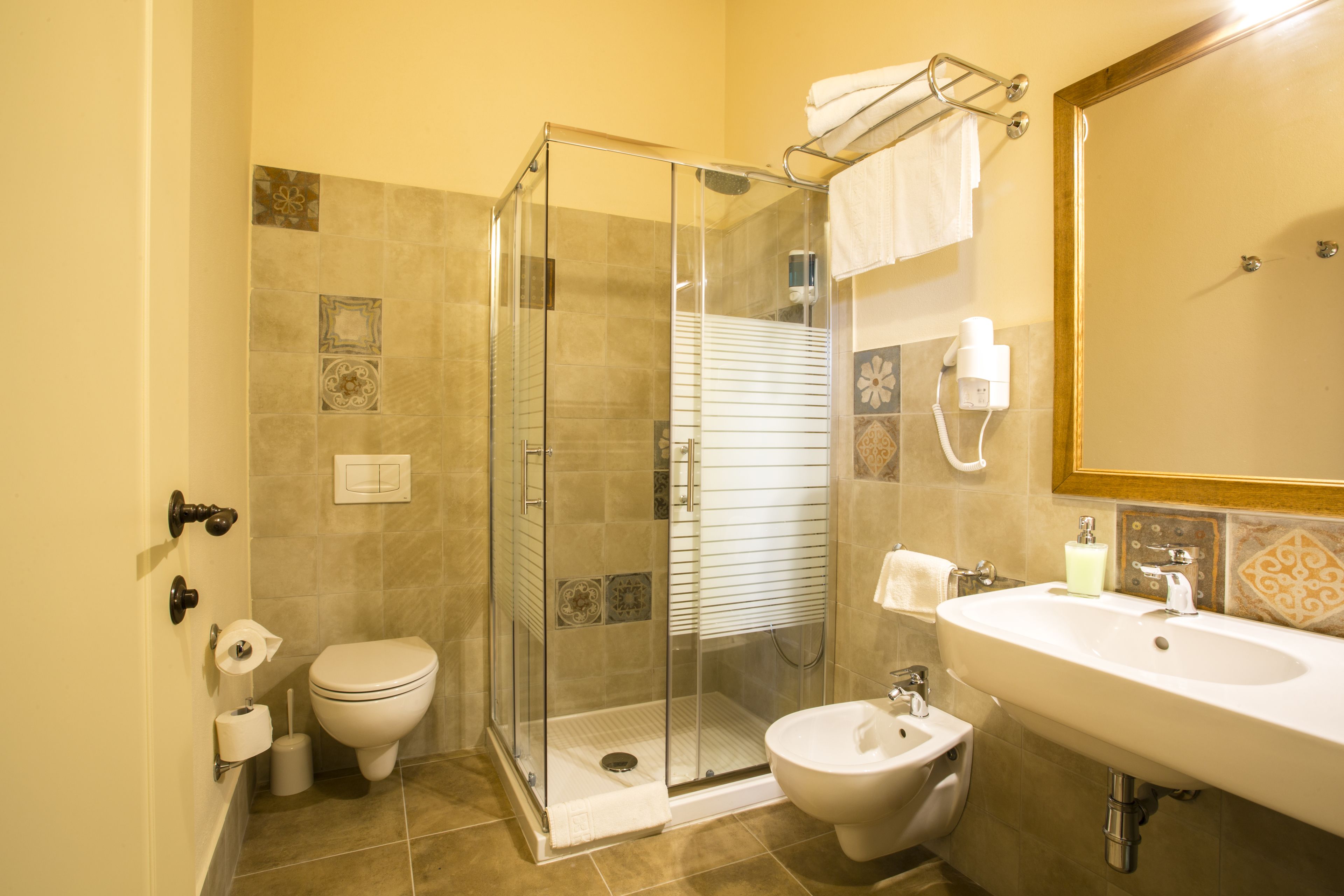 A bathroom with a glass-enclosed shower, a toilet, a bidet, and a sink with a mirror.