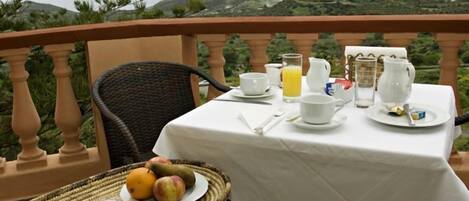 A table set for breakfast with croissants, fruit, and juice, overlooking a scenic landscape.