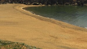 Un paisaje costero con una playa arenosa, una colina cubierta de hierba y un promontorio rocoso.