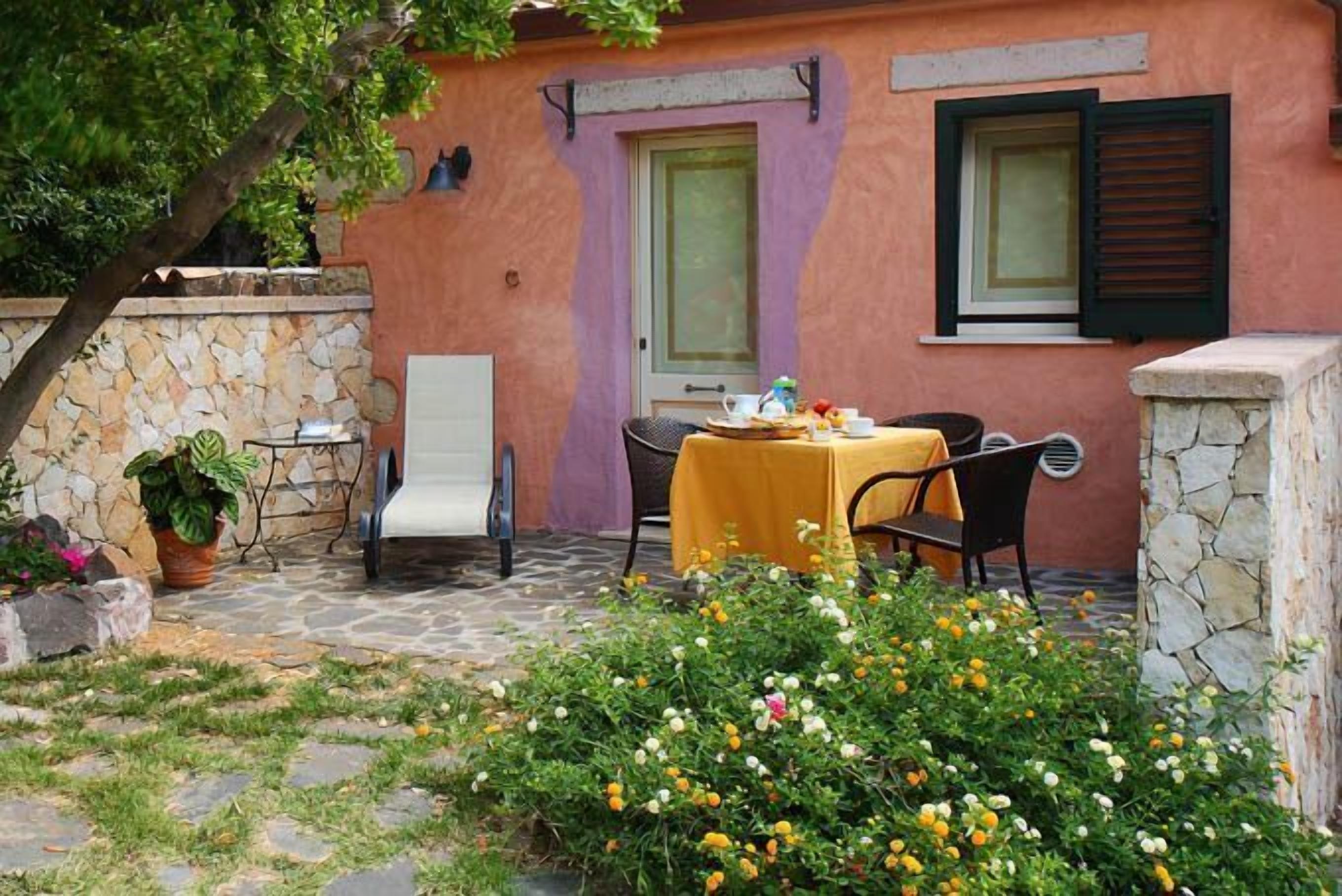 A stone patio with a table set for two, surrounded by a garden with various flowers.