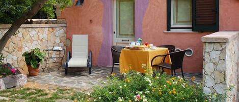 Un patio de piedra con una mesa dispuesta para dos personas, rodeado de un jardín con diversas flores.