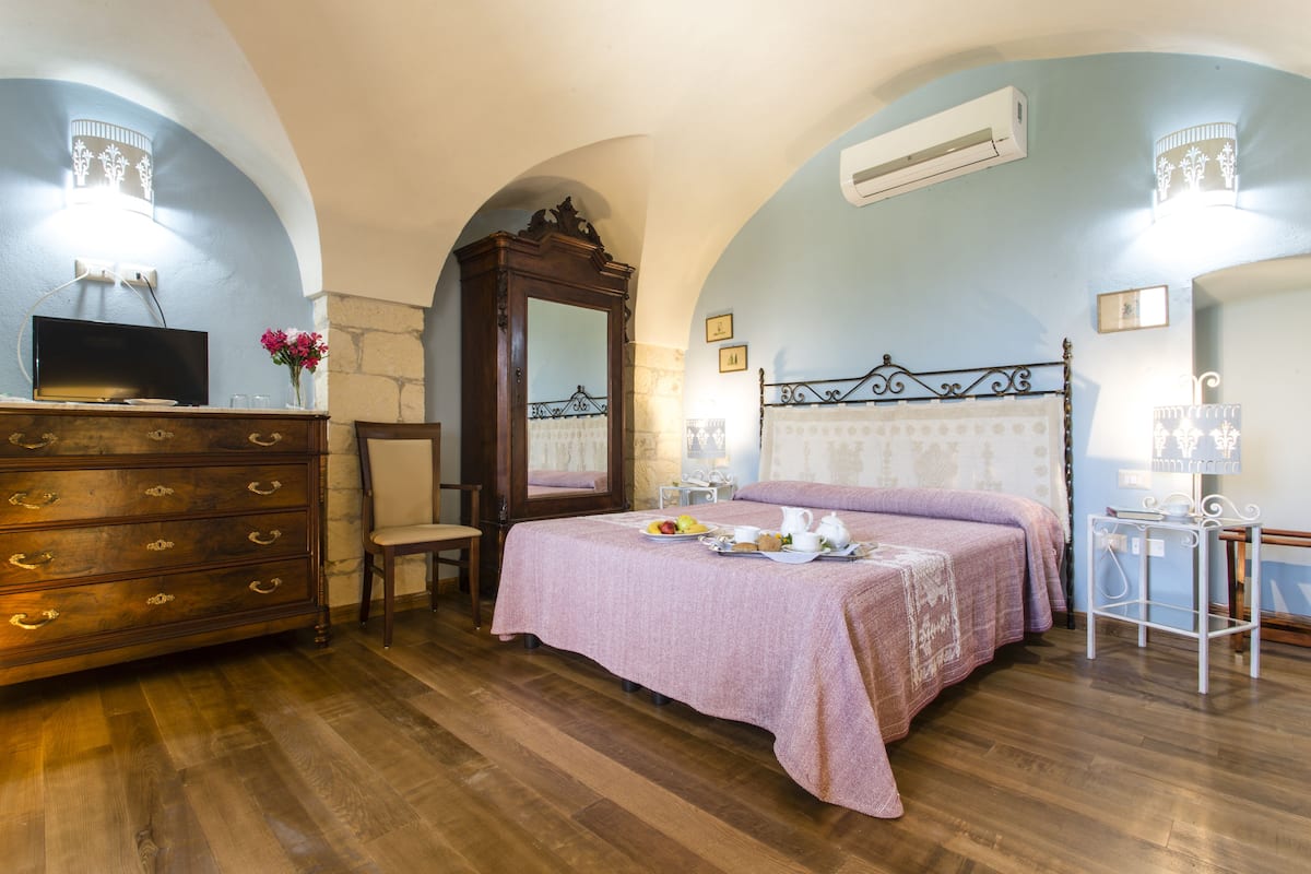 A bedroom with a wooden dresser, a bed with a pink bedspread, a mirror, and a television on a dresser.