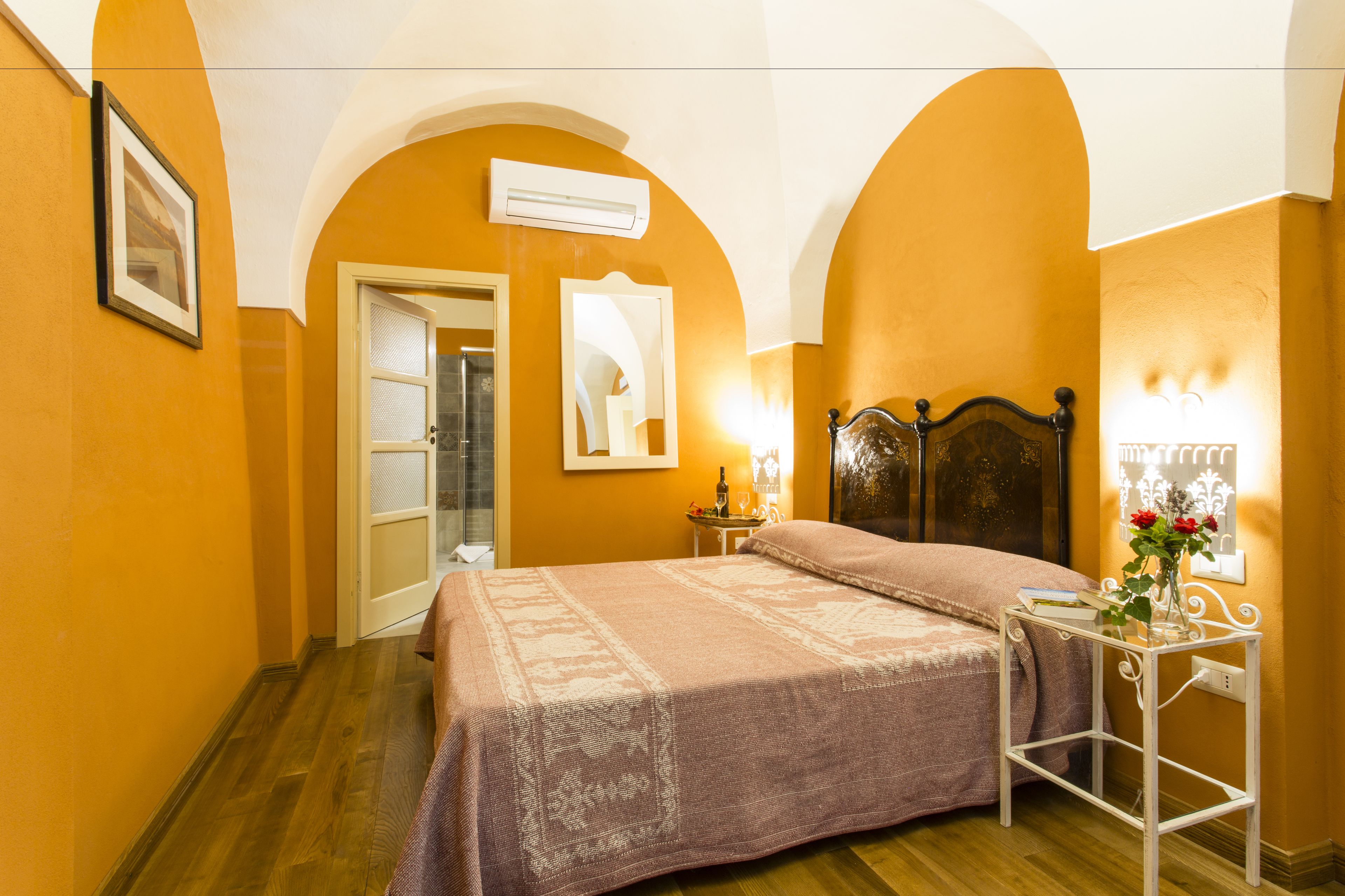 A bedroom with a bed, a bedside table with a lamp, a mirror, and a picture on the wall.