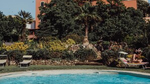 Piscina con sillones de descanso, rodeada de abundante vegetación y un muro de piedra.