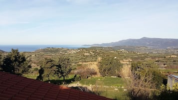 A view of a coastal landscape with a clear sky, a distant sea, and a hilly terrain with scattered buildings.