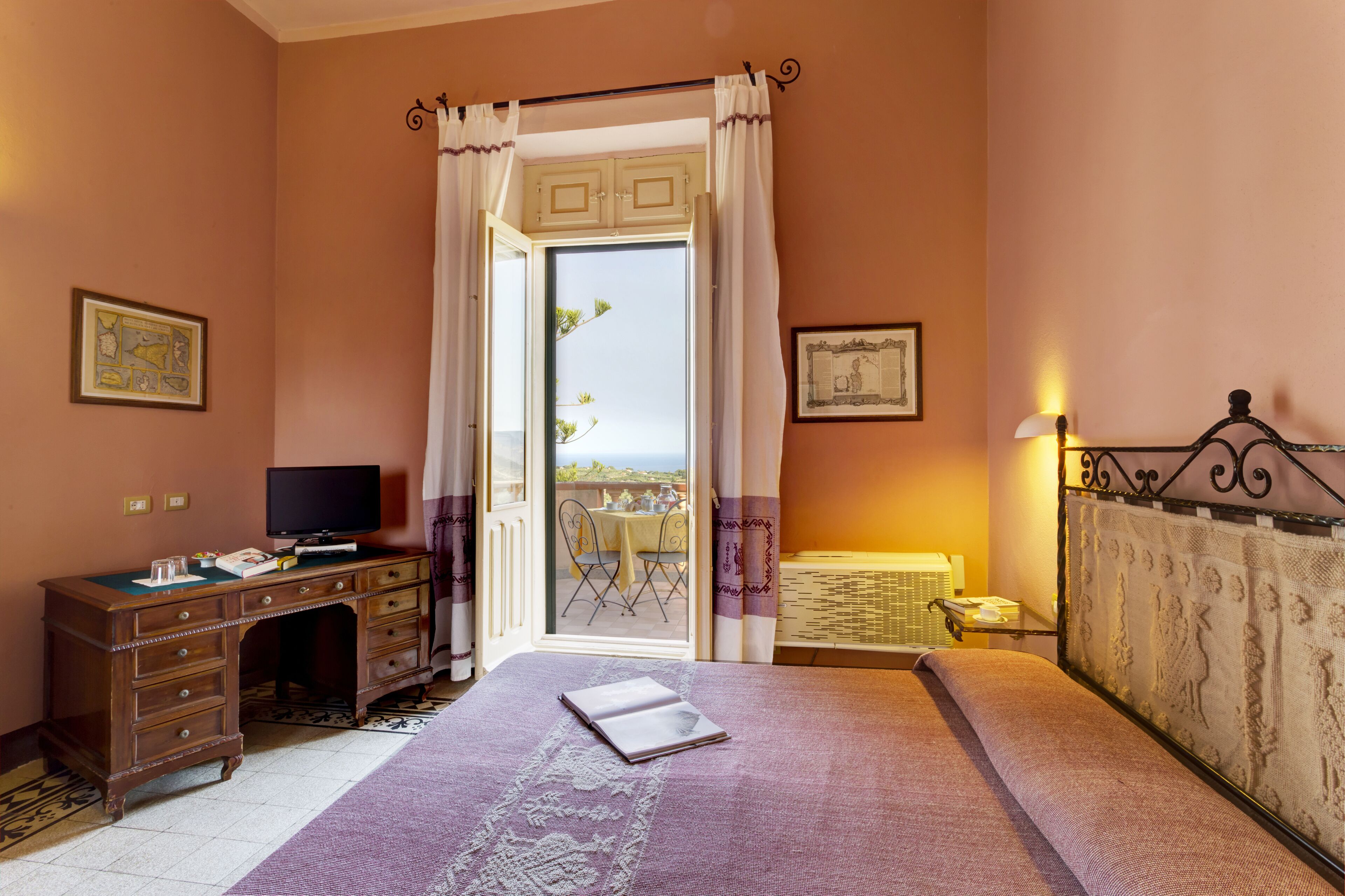 A bedroom with a bed, a desk, a television, and a balcony with a table and chairs.