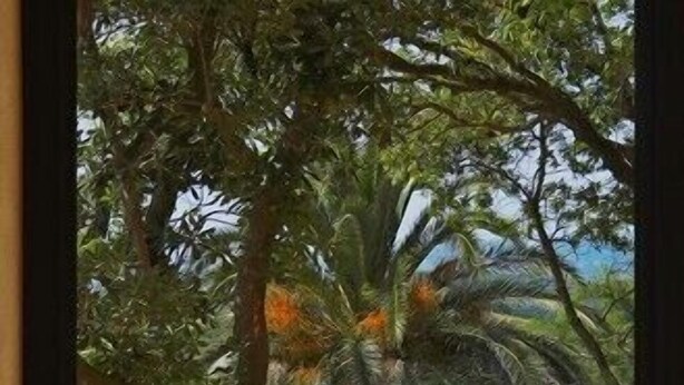 Una mesa con una cesta trenzada, una jarra y dos tazas, frente a una ventana con vistas a una piscina y exuberante vegetación.