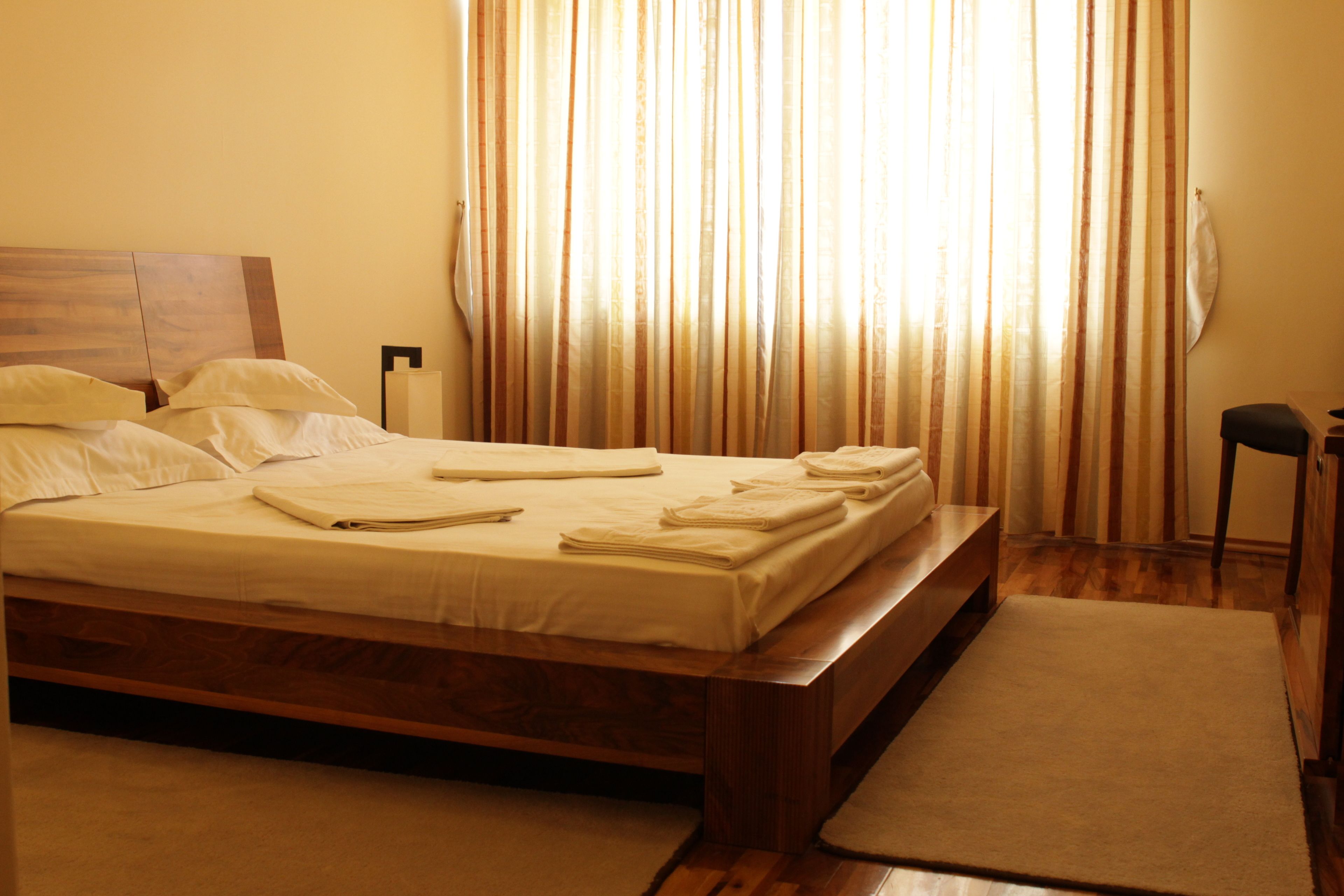 A neatly made bed with white linens and towels, a wooden headboard, and a bedside table with a lamp.