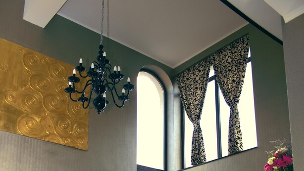 Un hall d’entrée spacieux, agrémenté d’un lustre, de grandes fenêtres avec des rideaux à motifs et offrant une vue sur l’extérieur.
