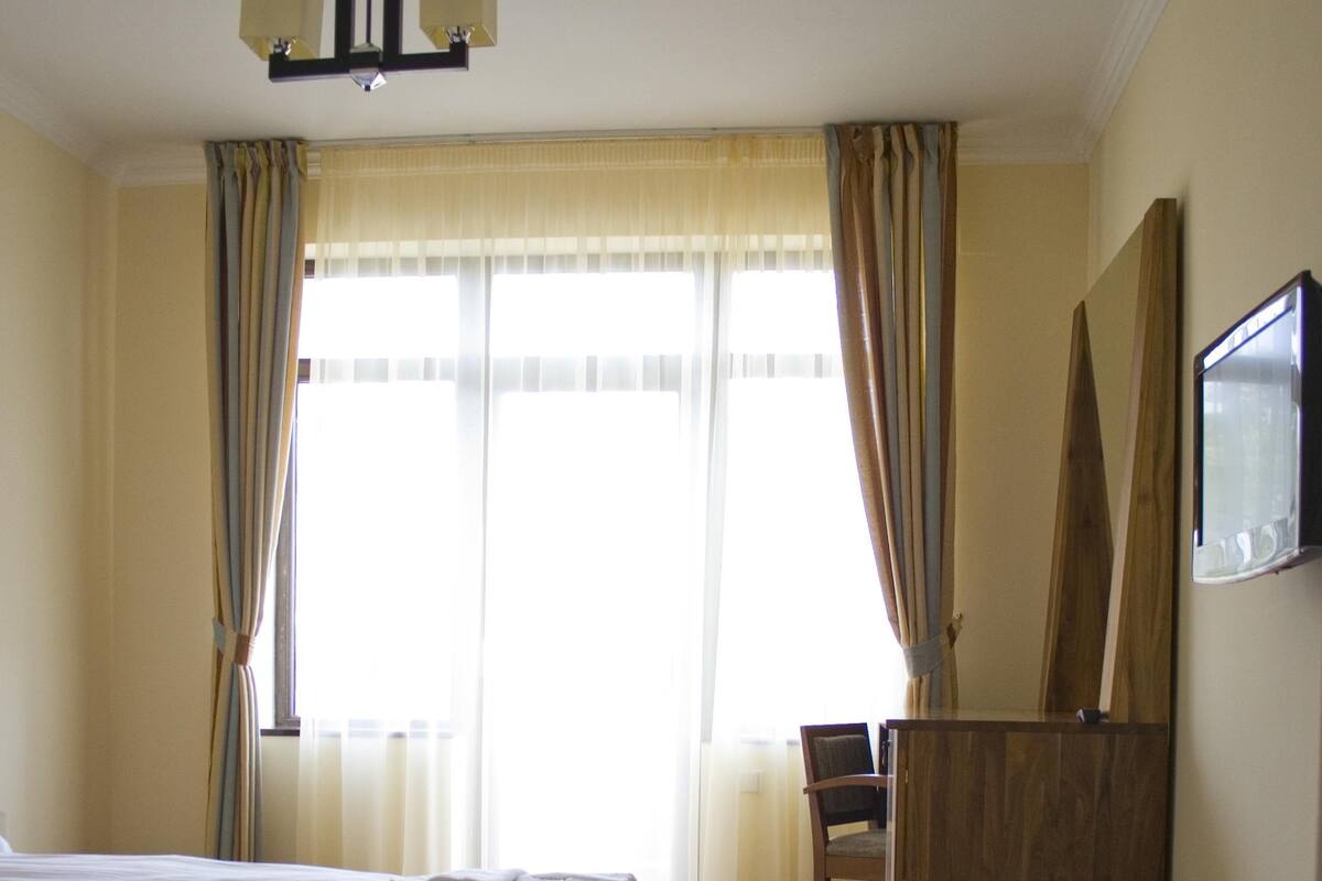 A hotel room with a bed, a desk, a chair, a TV, and a window with curtains.