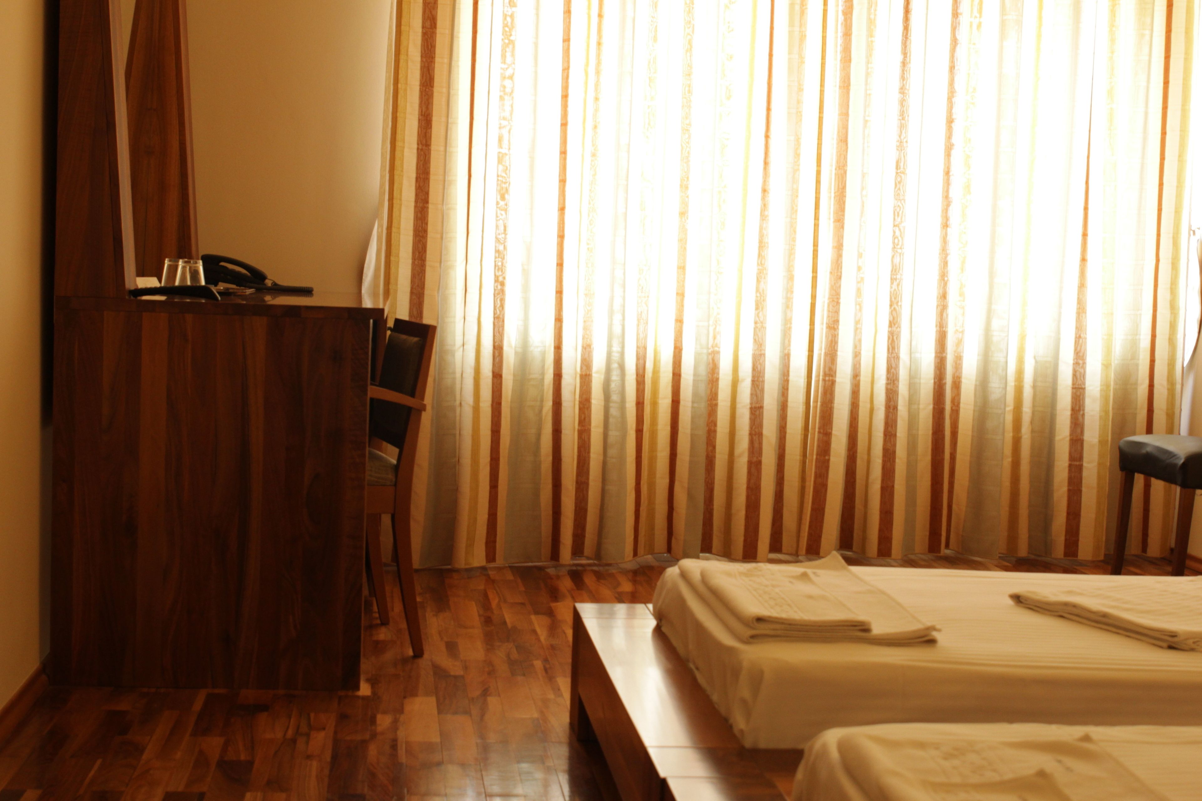 A hotel room with a wooden desk, two beds, and a large window with striped curtains.