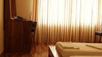 A hotel room with a wooden desk, two beds, and a large window with striped curtains.