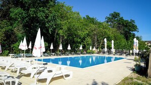Une piscine entourée d’arbres, avec des chaises longues blanches et des parasols.