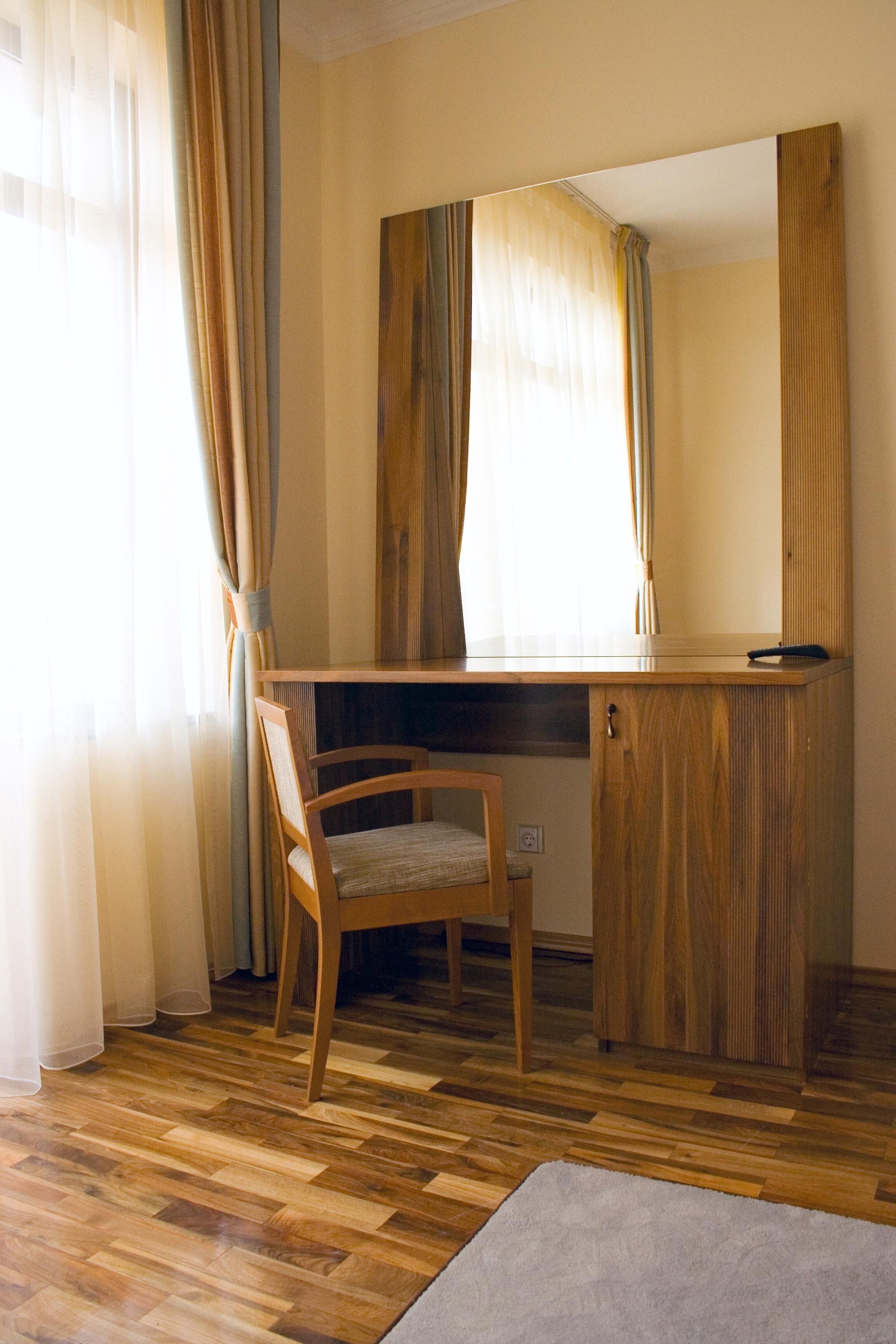 A room with a wooden desk, a chair, a mirror, and a window with curtains.