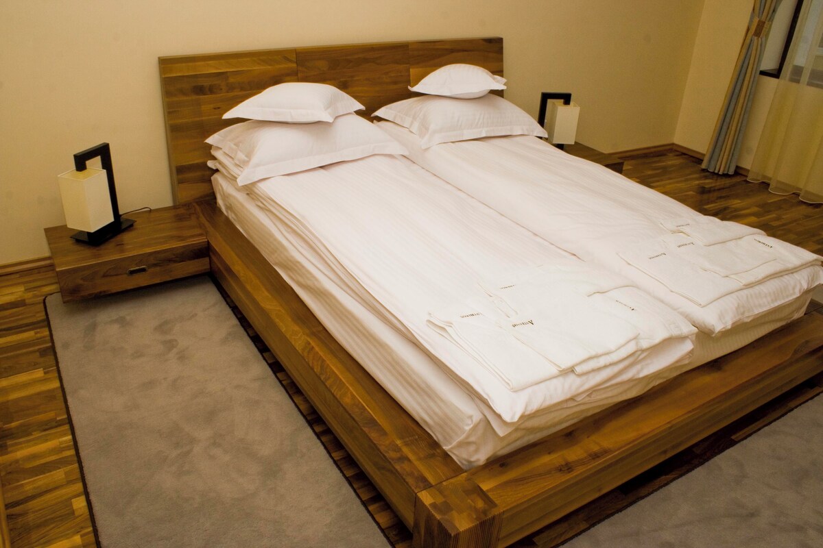Un lit double avec du linge de lit blanc, deux tables de chevet avec des lampes et une tête de lit en bois.