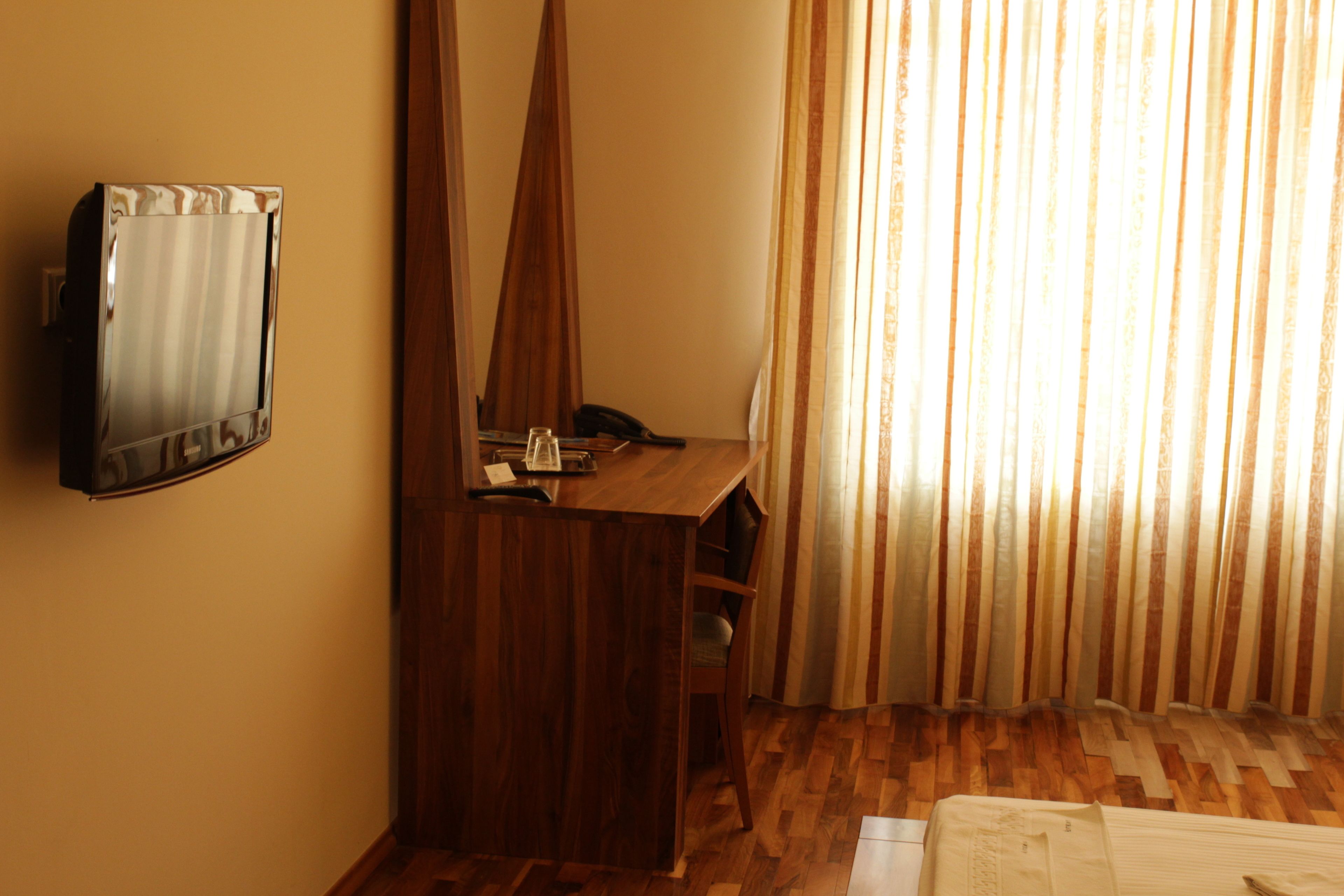 A hotel room with a wooden desk, a telephone, and a wall-mounted TV.