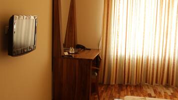 A hotel room with a wooden desk, a telephone, and a wall-mounted TV.