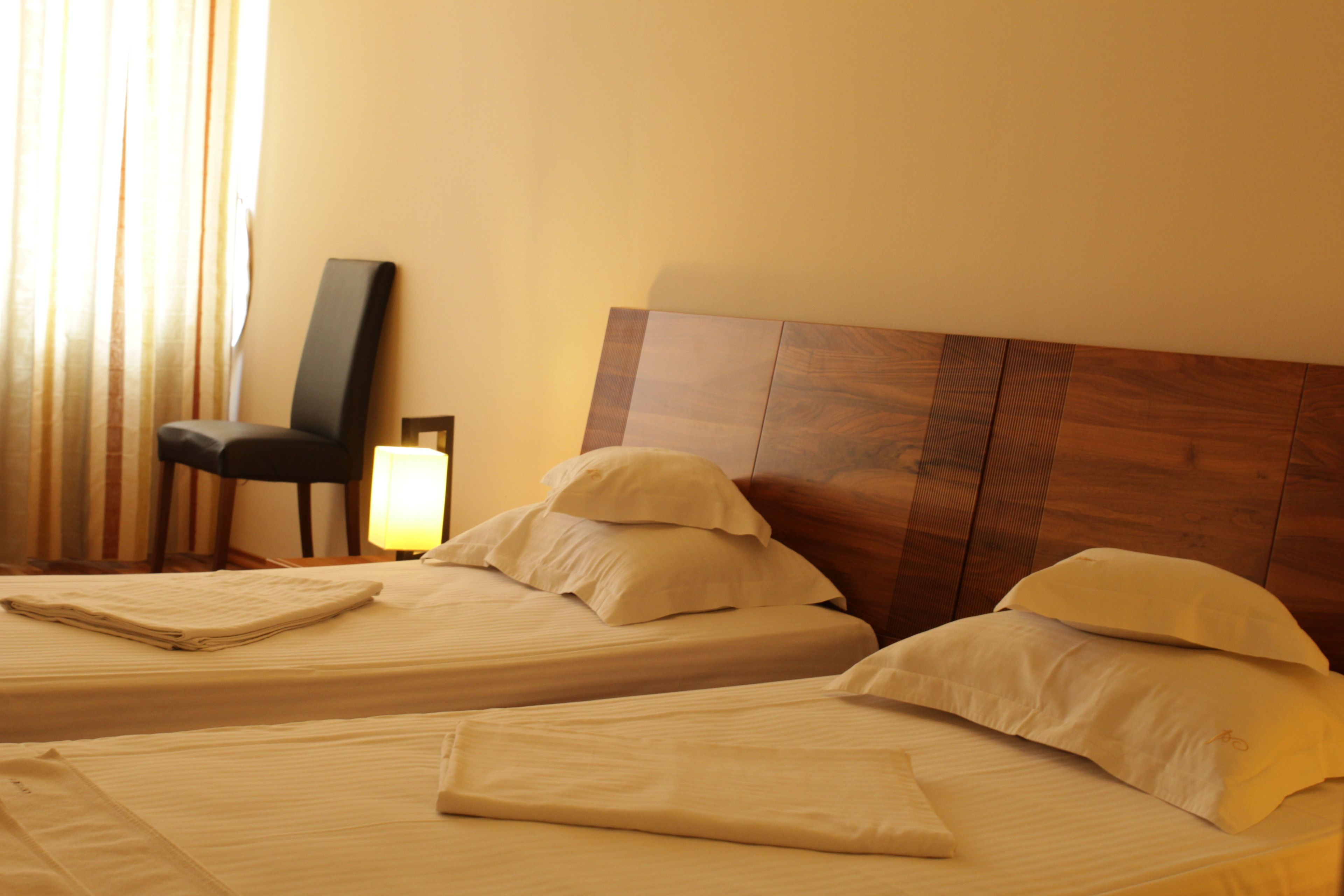A hotel room with two beds, a wooden headboard, a chair, and a lamp.