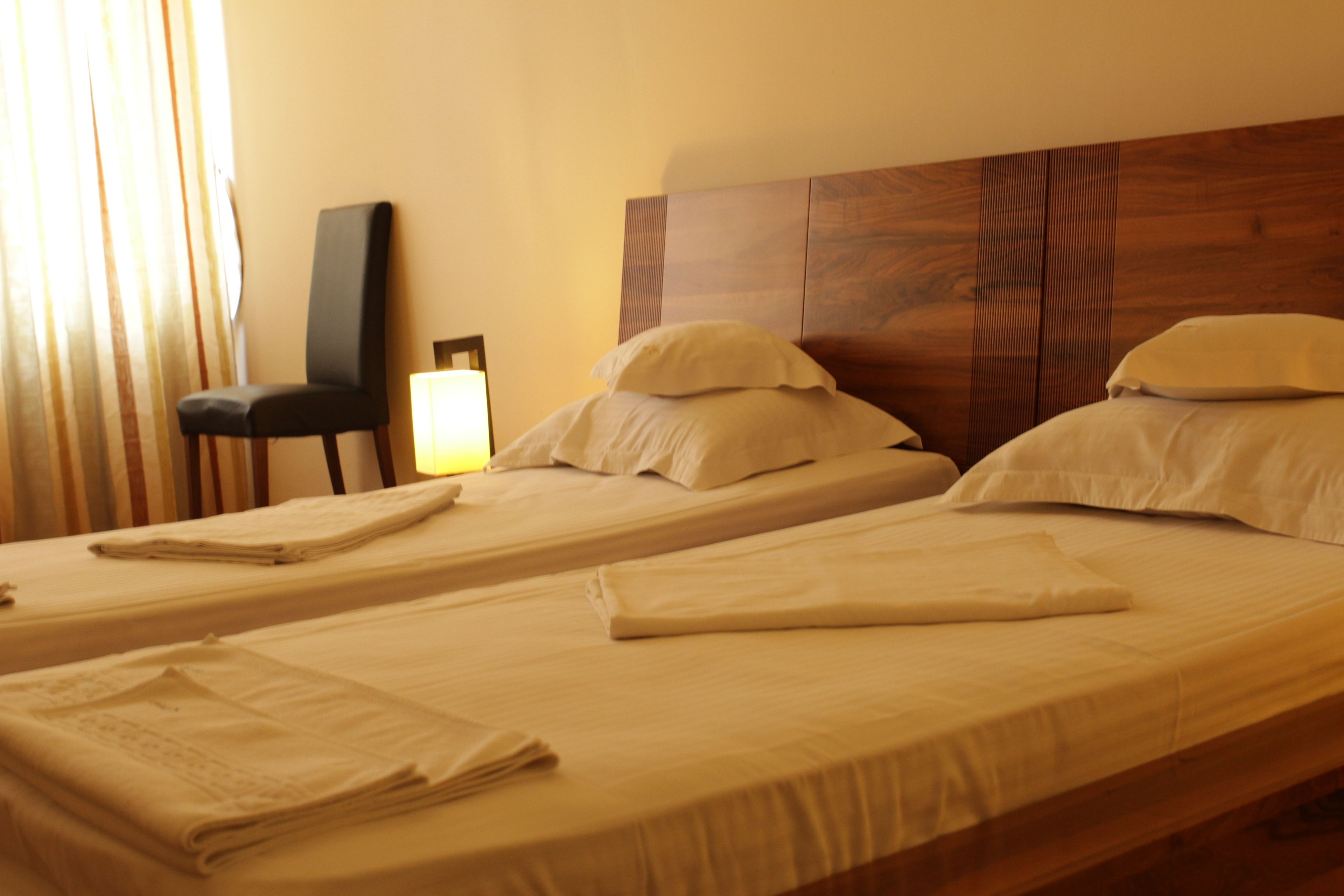 Ein Hotelzimmer mit zwei Einzelbetten, einem Holzkopfteil, einem Sessel und einer Lampe.