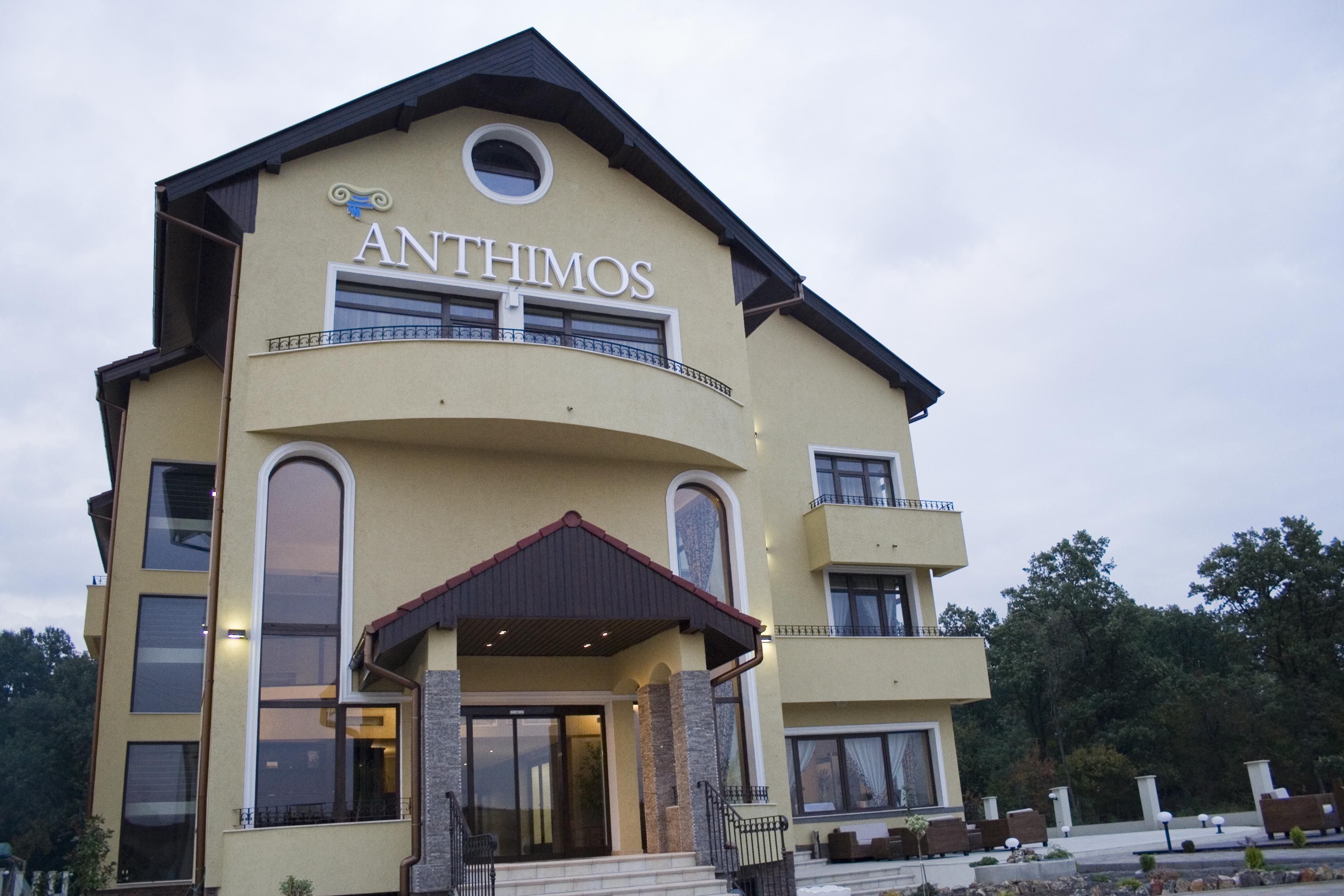 A multi-story building with the name "ANTHIMOS" prominently displayed. It features large windows, a covered entrance, and a balcony on the upper floor.