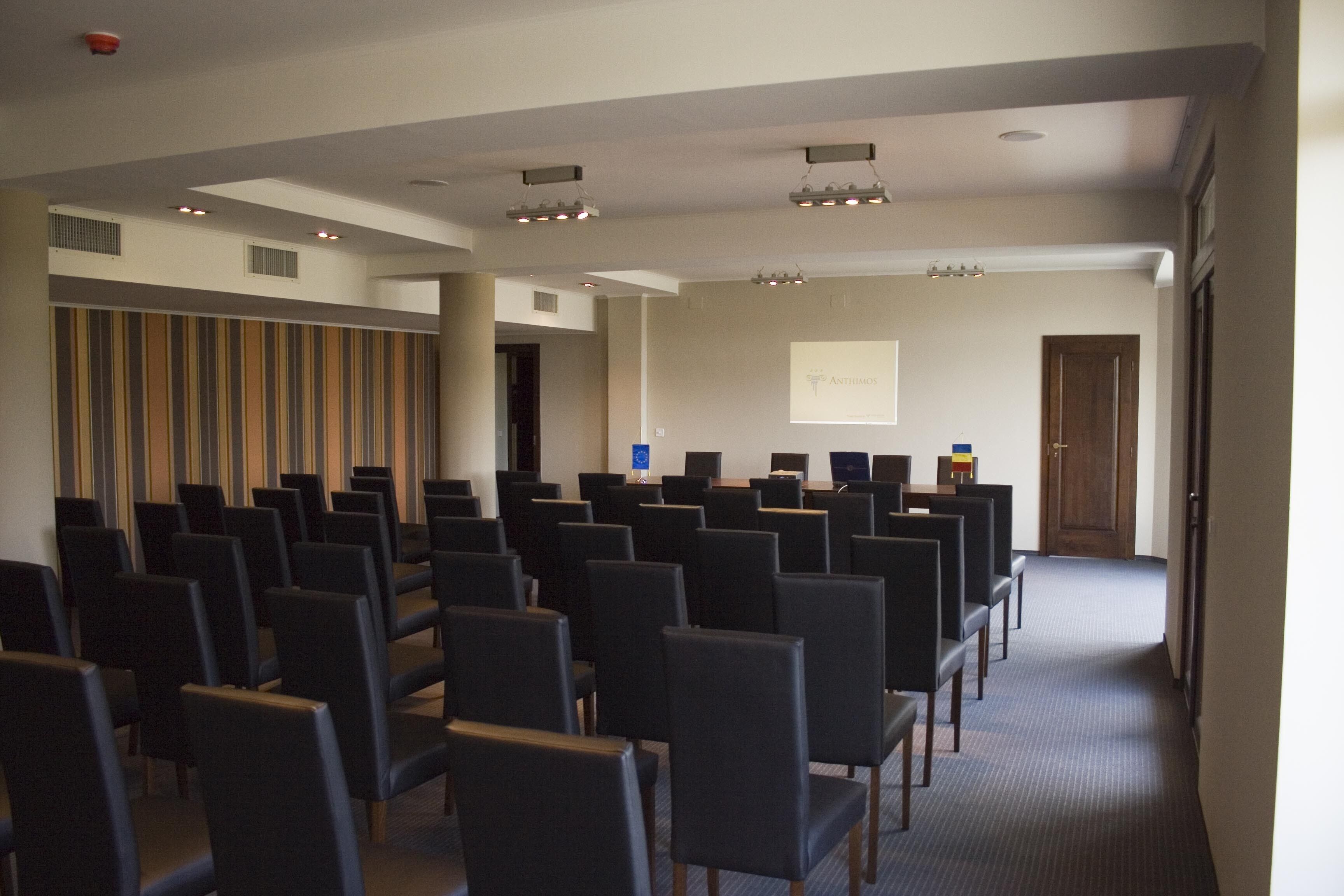 Une salle de conférence avec des rangées de chaises, un écran de projection et un pupitre.